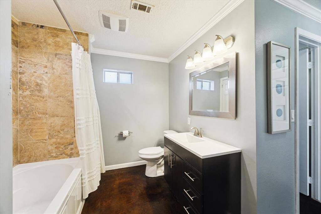 Primary bathroom features natural stone tile with a sleek vanity and tub-shower combo.