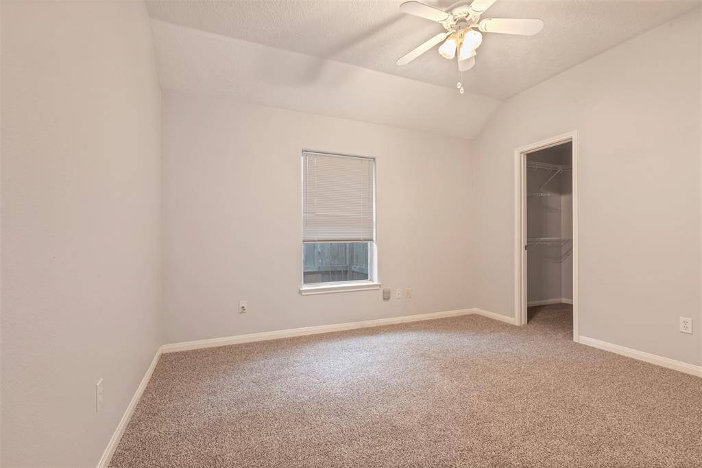 This room features neutral walls and carpet, a ceiling fan with lights, a window with blinds, and a walk-in closet, offering a cozy and functional space.