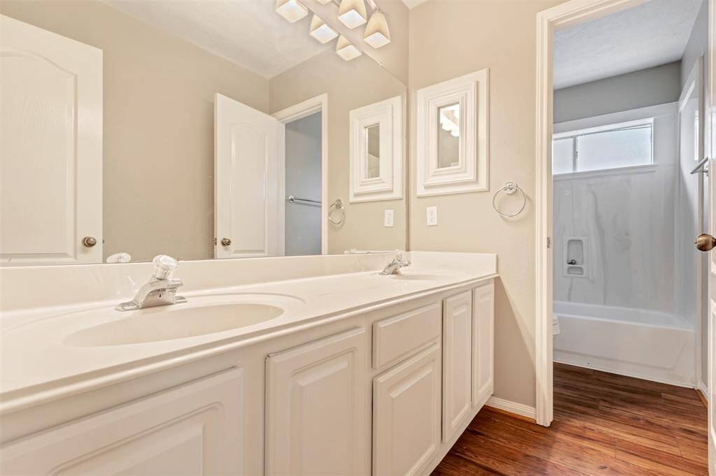 This bathroom features a double-sink vanity with ample storage, a large mirror, and modern lighting. It has a separate shower and tub area, complemented by wood-look flooring and neutral wall colors.