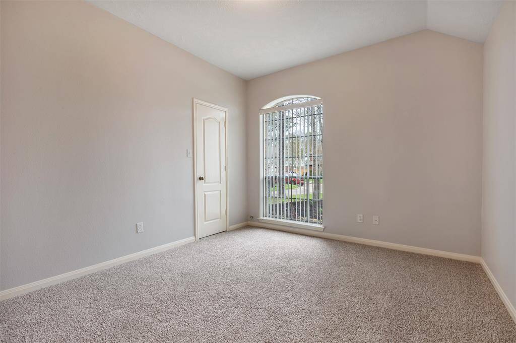 This room features a soft carpeted floor, neutral walls, and a large window with vertical blinds, allowing natural light to fill the space. A single door provides access, making it ideal for a cozy bedroom or office.