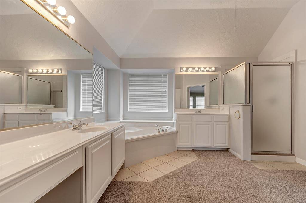 Spacious bathroom with dual sinks, a large vanity mirror, a corner bathtub, and a separate shower. Features carpet and tile flooring, bright lighting, and ample natural light from a large window.