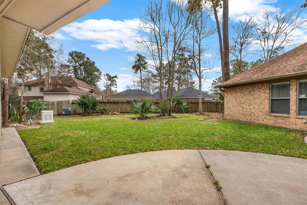 This photo showcases a spacious backyard with a well-maintained lawn, surrounded by a wooden fence and mature trees. The area is complemented by a concrete patio, offering ample space for outdoor activities and relaxation.