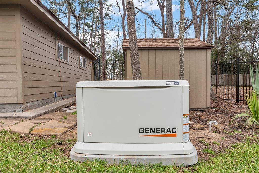 The photo shows a Generac home generator installed in a backyard, providing reliable backup power. It's positioned on a neatly maintained lawn next to a brown shed and a house, surrounded by trees and a fence.