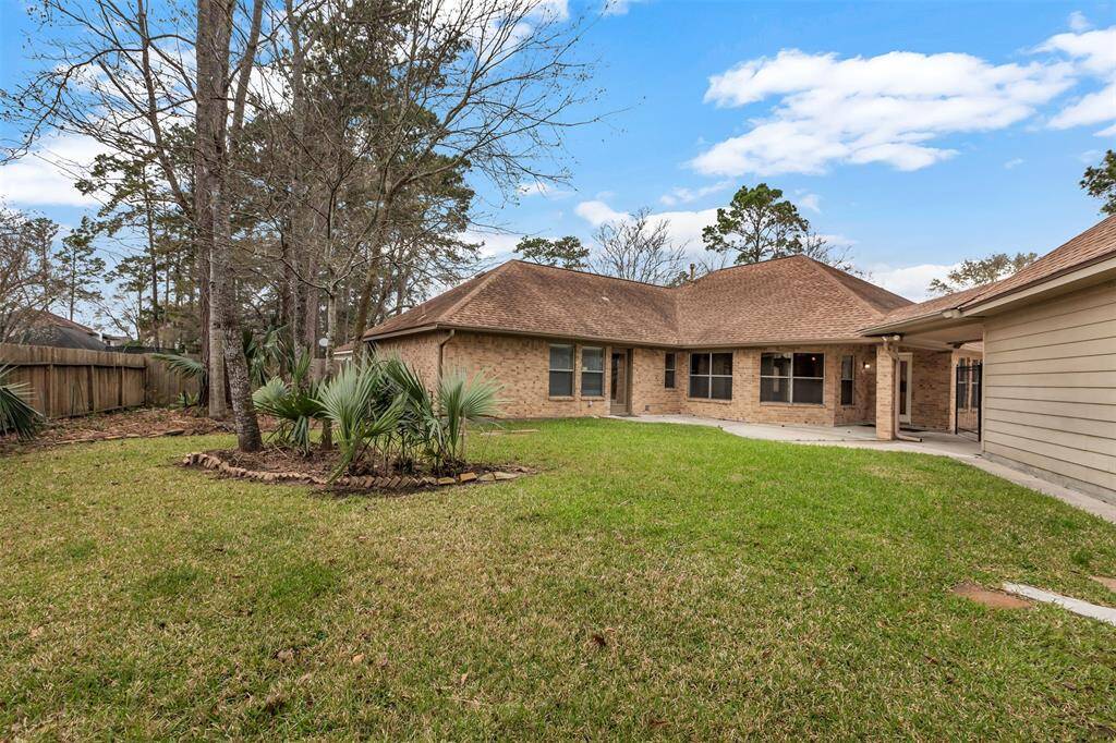 This photo showcases a charming brick home with a spacious, well-maintained backyard. The yard features mature trees and a small garden area, providing a serene outdoor space. The house has a covered patio and large windows, ideal for natural light and outdoor enjoyment.