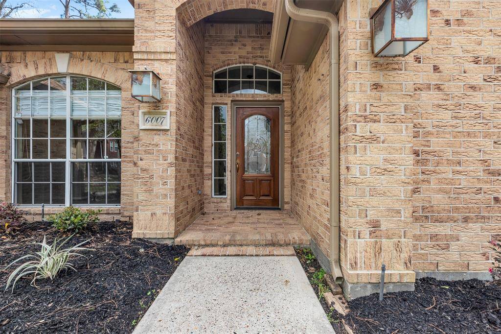 This photo showcases an inviting front entryway with a classic brick exterior. It features a wooden front door with decorative glass, framed by arched windows. The well-maintained landscaping adds curb appeal to this welcoming home entrance.