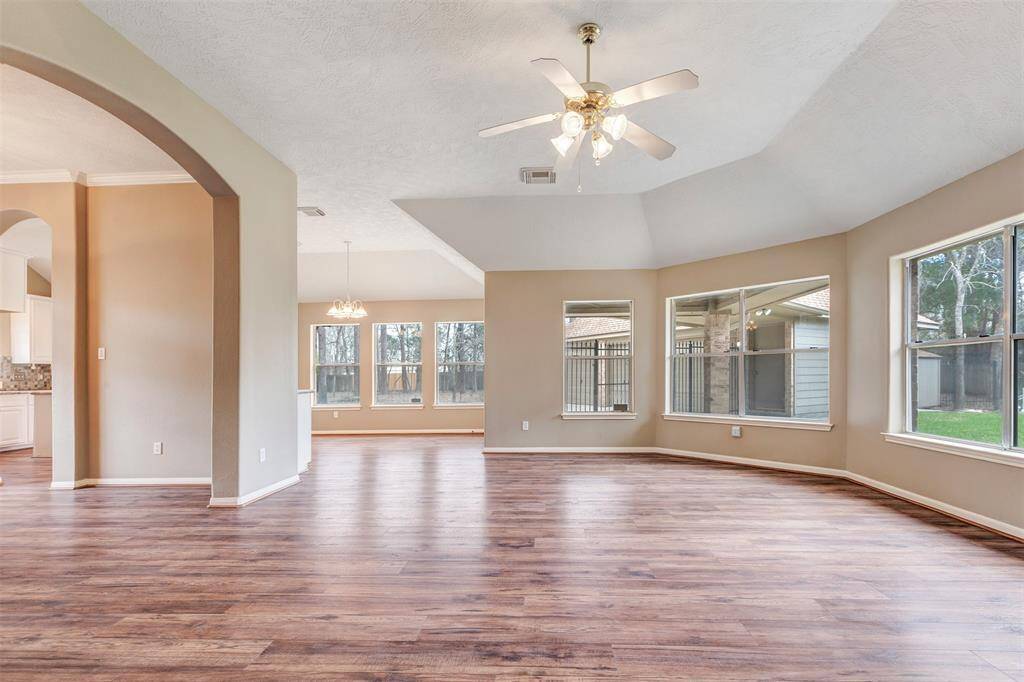 Spacious living area with wood flooring, large windows offering plenty of natural light, and an open layout connecting to the dining area and kitchen. Features a ceiling fan and neutral wall colors.