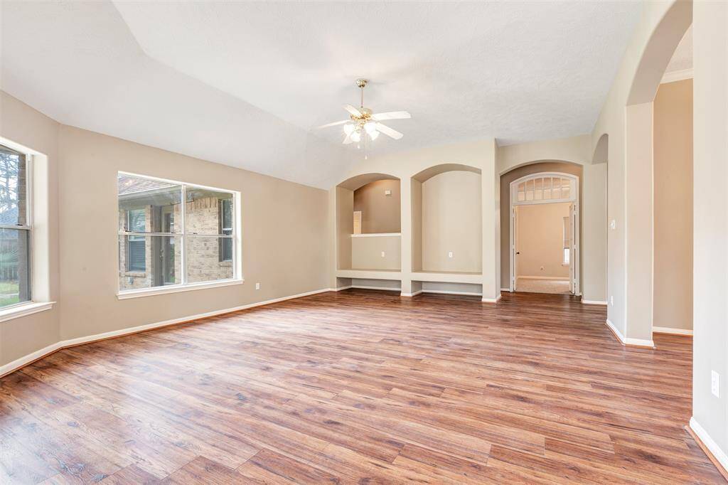 This spacious living area features elegant hardwood flooring, neutral walls, and large windows that provide ample natural light. The room includes a ceiling fan and charming archways, leading to other parts of the home, creating an inviting and open atmosphere.