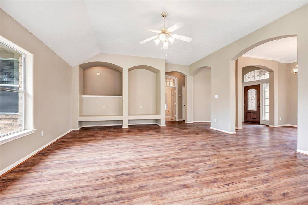 This spacious living area features elegant wood flooring, neutral walls, and large arched doorways, creating an inviting and open atmosphere. Natural light streams through ample windows, highlighting the architectural details and high ceilings.