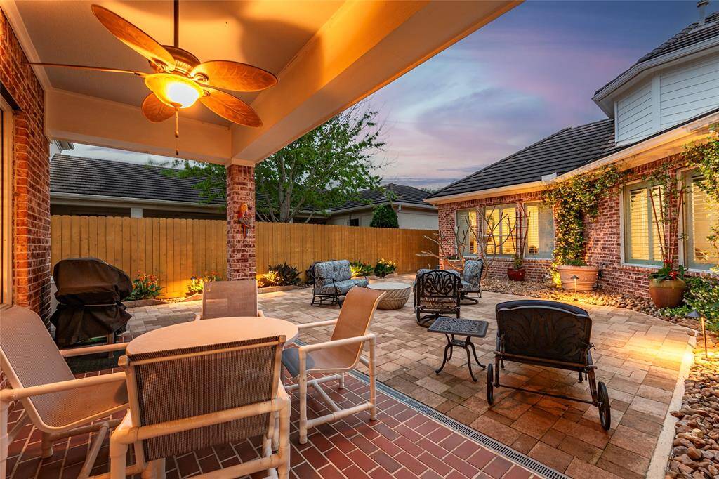 Charming backyard patio with recent 7-foot fence, cozy seating, ceiling fan, and warm lighting. Brick paver design, surrounded by lush greenery, creating a perfect space for your extended outdoor living.