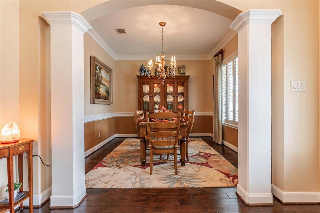This photo showcases an elegant dining room crown molding and chair-rail molding.  The room is framed by an archway and has large windows with plantation shutters.