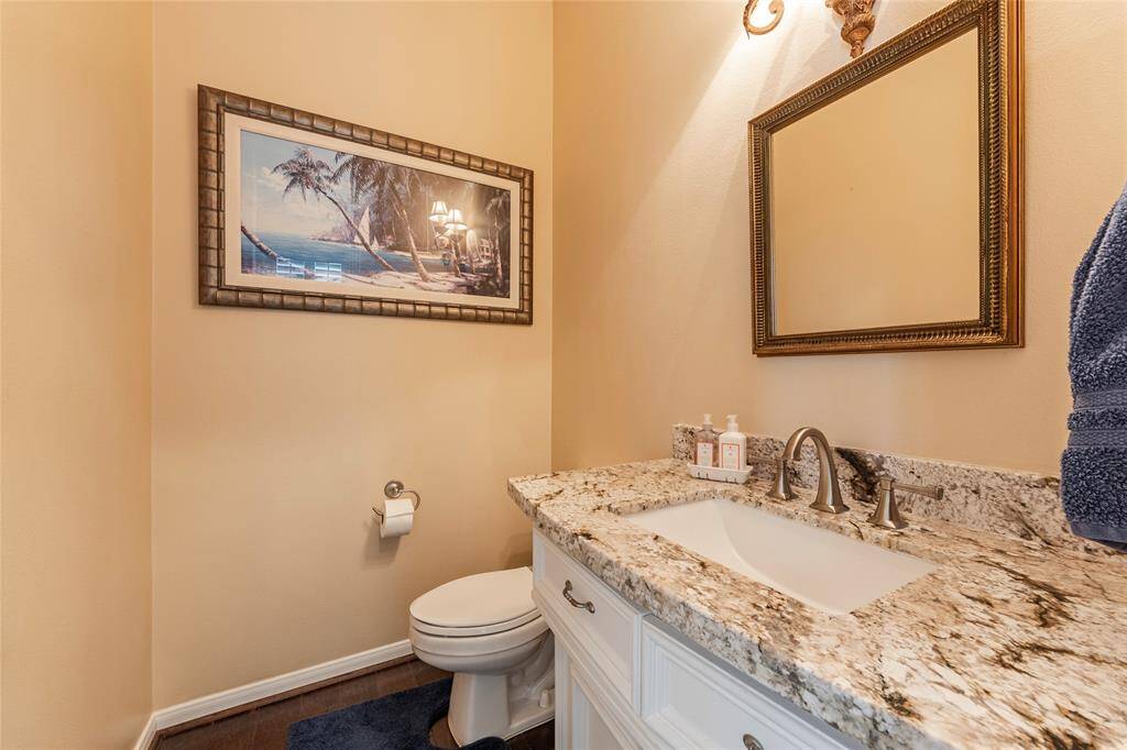Stylish powder room featuring granite countertop with undermount sink and elegant fixtures, complemented by a framed beach-themed artwork and decorative mirror.