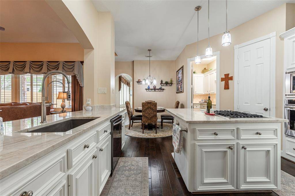 This photo showcases a spacious, open-concept kitchen and breakfast area with elegant white cabinetry, a large island with a gas cooktop, and pendant lighting.
