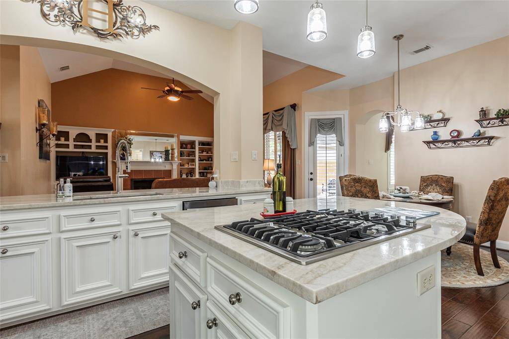 Stunning spacious kitchen with 3mm Quartzsite counter island featuring a built-in gas cooktop. The room is well-lit with pendant lights and opens to breakfast and family room.