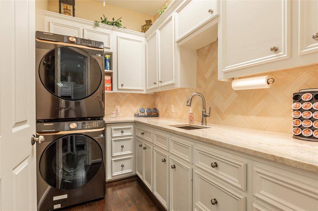 Well-organized laundry room featuring stacked washer and dryer set (included) with ample storage,  2nd sink, under-cabinet lighting and herringbone tile backsplash.