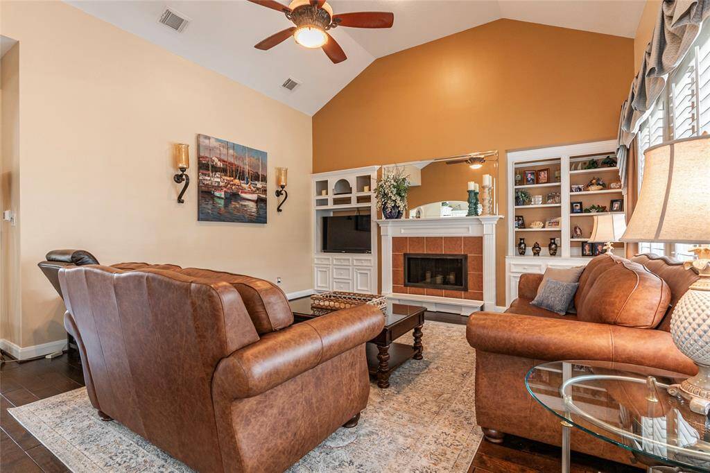 Family room features high vaulted ceilings, wood flooring, cozy gas fireplace with a white mantel and built-in storage and shelving.