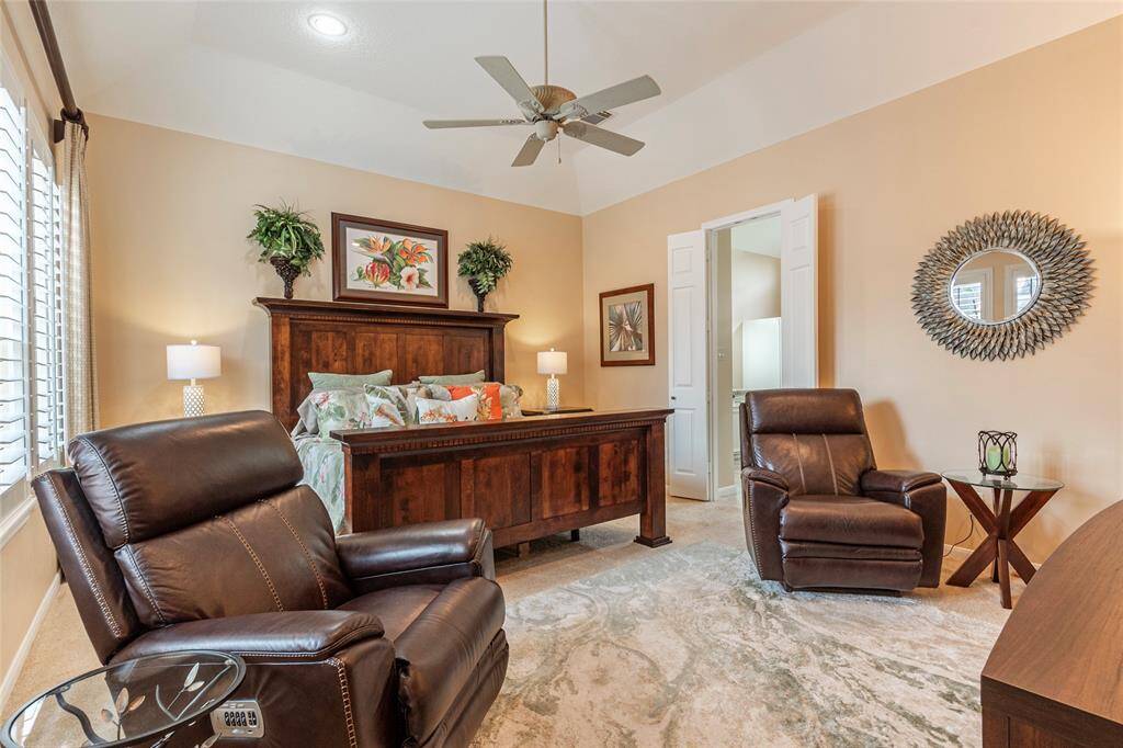 Primary bedroom features vaulted ceiling and ample natural light from large windows with shutters, creating a comfortable and inviting atmosphere.