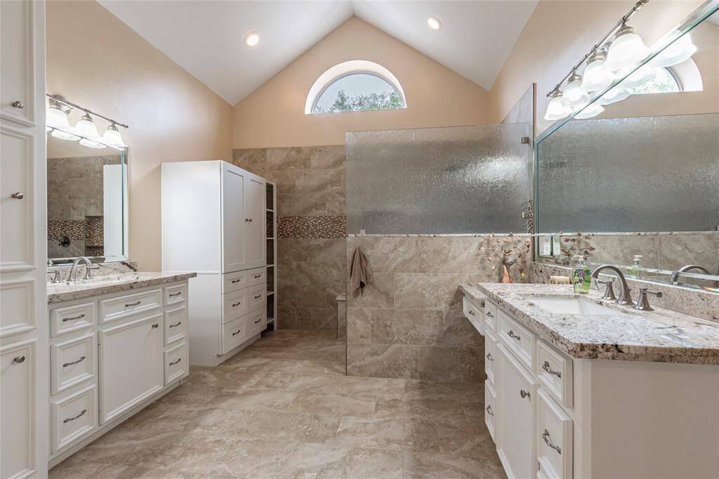 Renovated primary bathroom showcases granite countertops white cabinetry, upscale fixtures and a large walk-in shower. The room is well-lit with modern fixtures and has a serene, neutral color palette.
