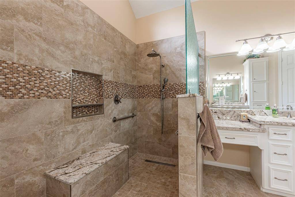 The ultimate spacious walk-in shower with a built-in bench and modern fixtures. The walls and floor are adorned with elegant stone tiles, complemented by a mosaic accent.