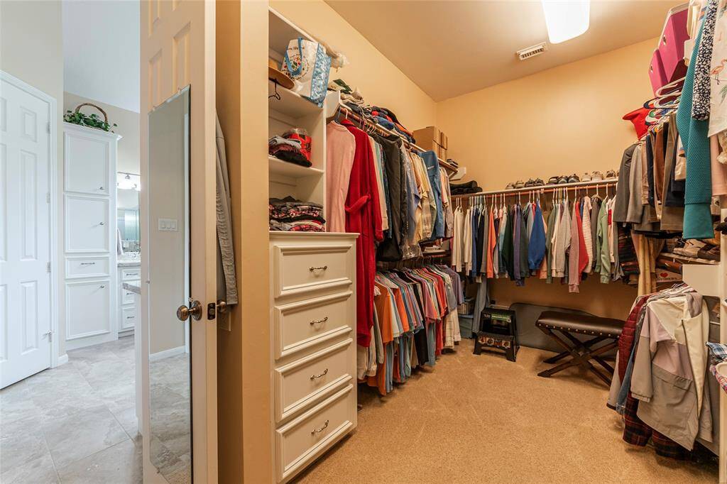 Spacious walk-in closet featuring storage drawers,  shelving and ample hanging space for clothes. It connects to a well-lit bathroom offering convenience and style for any homeowner.