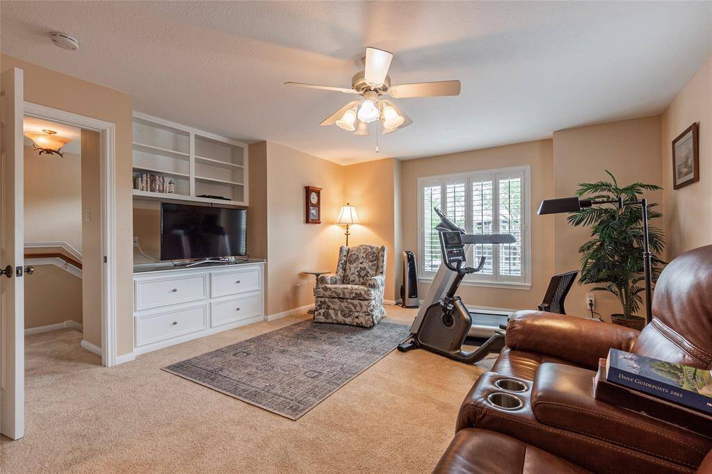 This upstairs 4th bedroom or additional versatile space features built-in entertainment center, full closet, half-bathroom and large windows with shutters for natural light. A ceiling fan and neutral tones add to the inviting atmosphere, perfect for relaxation or a home workout.