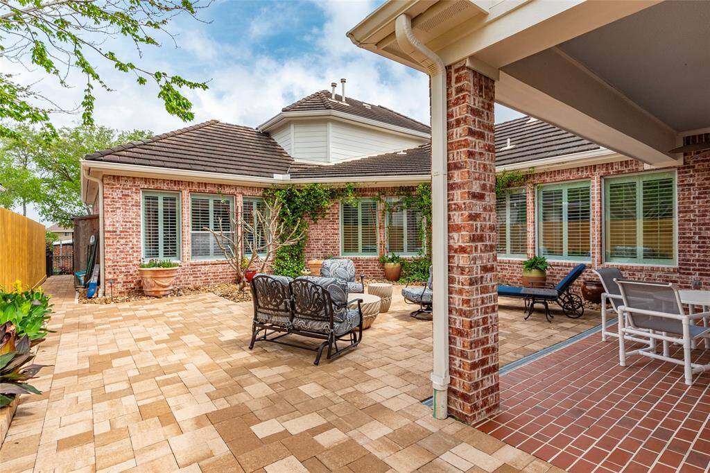 Spacious, brick-paved patio area with outdoor seating, surrounded by red brick walls and large windows. The space is enhanced with potted plants, creating an inviting atmosphere for relaxation or entertaining.