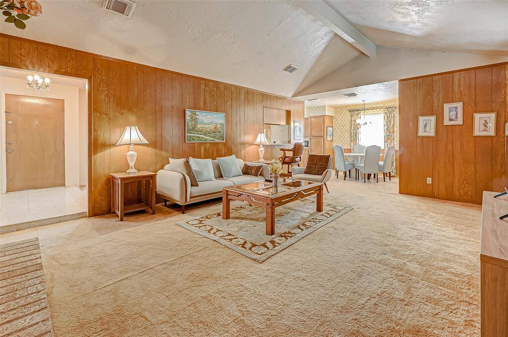 Spacious and open-concept, this main living area features vaulted ceilings, wood-paneled walls, and clear sightlines into the formal dining room. The layout is ideal for entertaining, with easy movement between lounging and dining spaces.