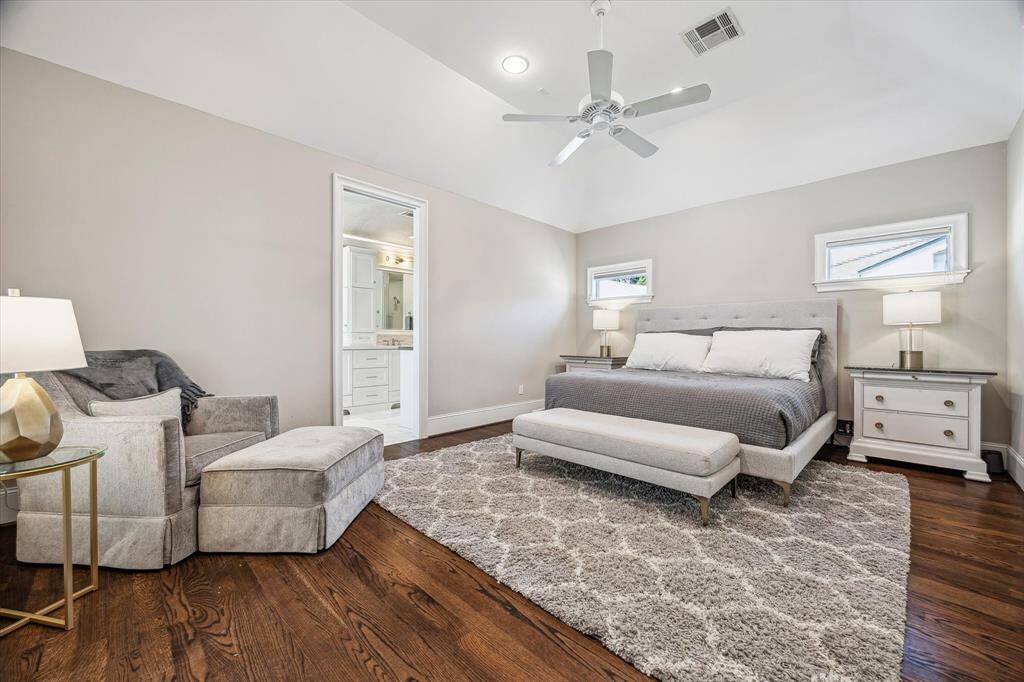 Welcome to the first-floor primary suite, featuring hardwood floors and an angled tray ceiling reaching 11 feet high. The bathroom is to the left, while a door to the right (not pictured) leads to the spacious walk-in closet and a private exercise room.