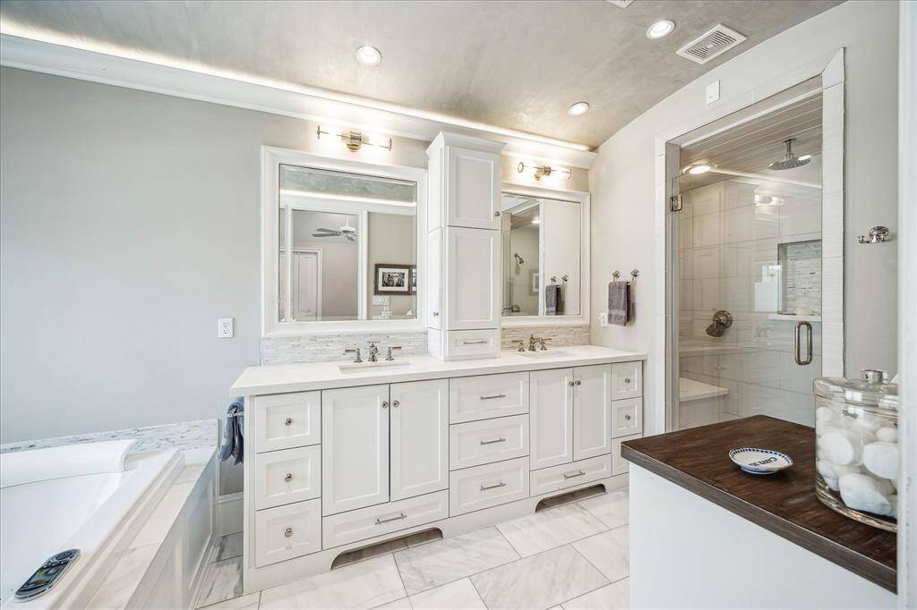 Experience luxury in the primary bathroom with a dual sink vanity offering ample storage, a smooth barrel-vaulted ceiling with lighting in the molding, a spacious glass shower with dual heads, and an oversized jacuzzi tub.