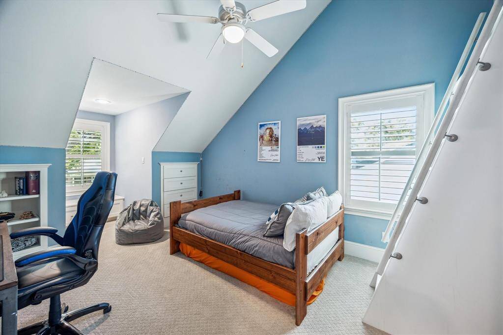 Explore one of the three upstairs bedrooms, featuring elegant plantation shutters, built-in shelving, ample storage, and vaulted ceilings.