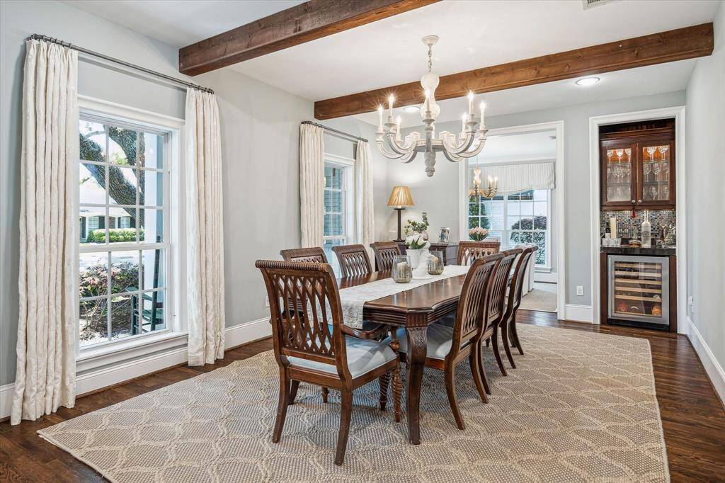 The formal dining room, located off the foyer, features large, light-filled windows, bold wooden ceiling beams, and a convenient dry bar with a beverage refrigerator and ample storage.