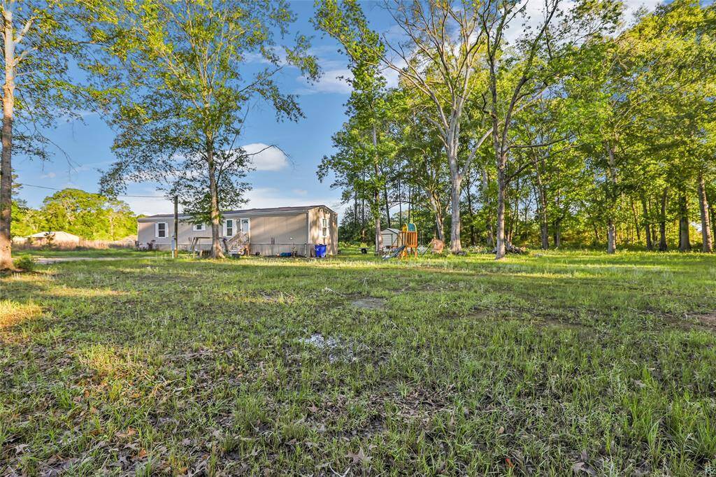 This photo showcases a spacious, grassy yard with mature trees, providing a serene and natural setting. A mobile home is visible in the background, offering a cozy living space. Ideal for those seeking privacy and a connection with nature.