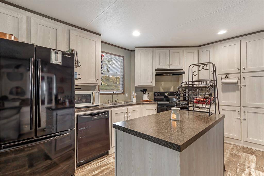 This kitchen features modern black appliances, ample cabinet space, and a central island for cooking and storage. The warm wood flooring and neutral cabinetry create a welcoming and functional space for any home chef.
