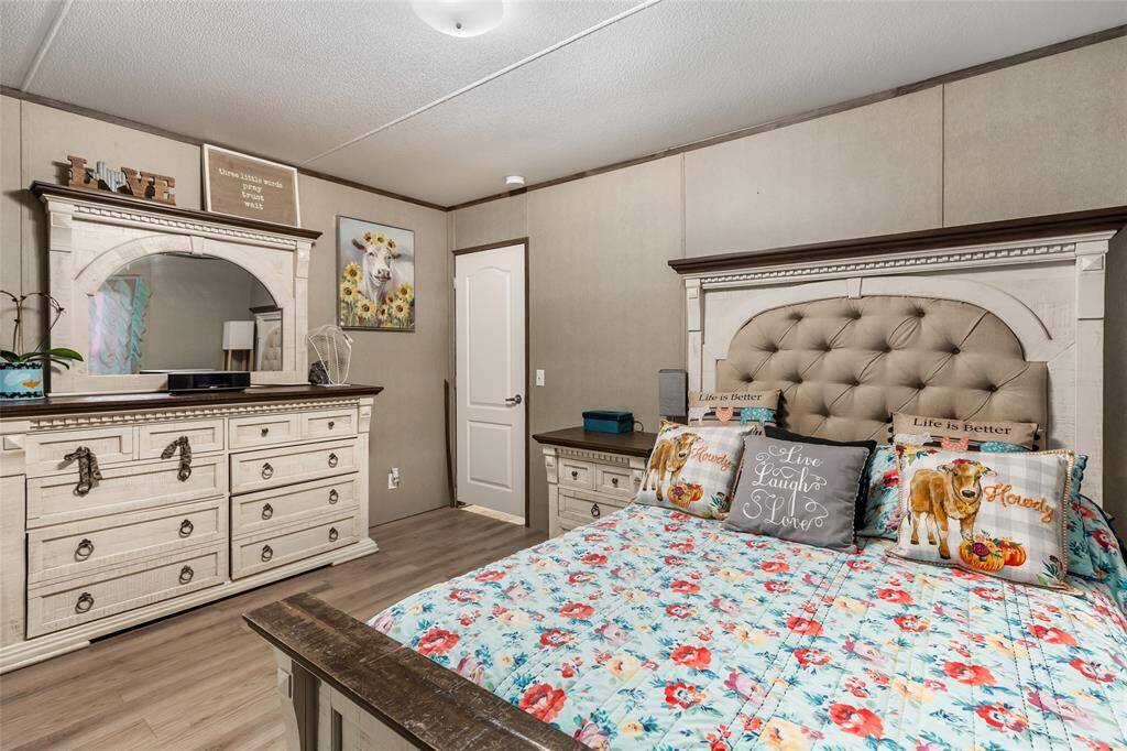 Comfortable bedroom with a rustic vibe, featuring a floral bedspread and decorative pillows. The room includes a large dresser with a mirror, light wood flooring, and charming wall art, creating a cozy and inviting space.