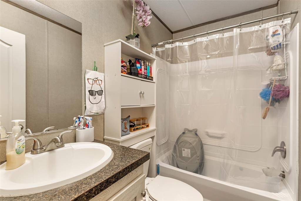 This bathroom features a compact layout with a bathtub-shower combo, a clear shower curtain, and a vanity with a dark countertop. It includes a wall-mounted cabinet for storage and neutral-colored walls, creating a practical and tidy space.