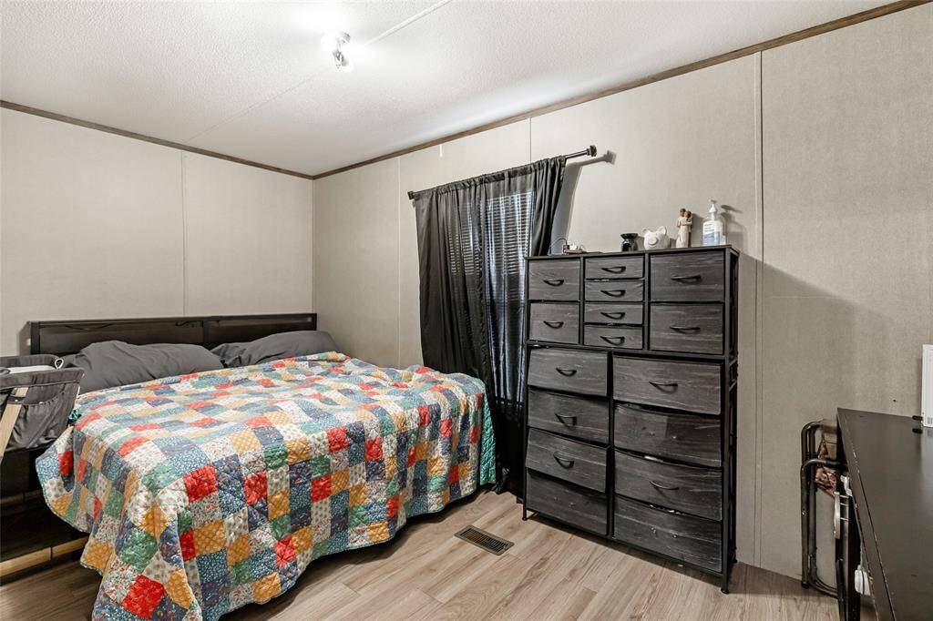 Cozy bedroom featuring a double bed with a colorful quilt, a spacious black dresser, and laminate flooring. A window with dark curtains adds light and privacy. Perfect for comfort and functionality.