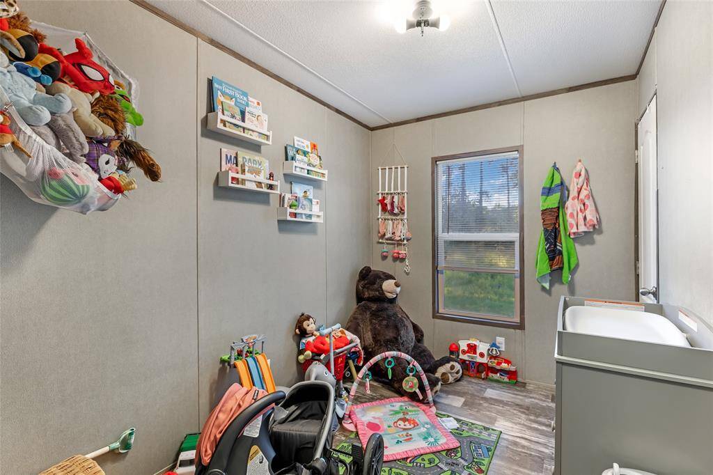 This cozy room is designed as a children's play and sleep area, featuring soft gray walls, a window with a view, and playful decor. It includes shelves for books and toys, a changing table, and ample space for activities. Perfect for a young family.