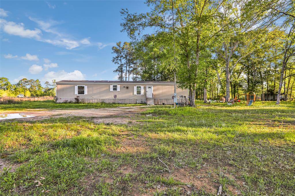 This photo shows a single-story mobile home set in a spacious, grassy yard with tall trees. The setting is quiet and surrounded by nature.