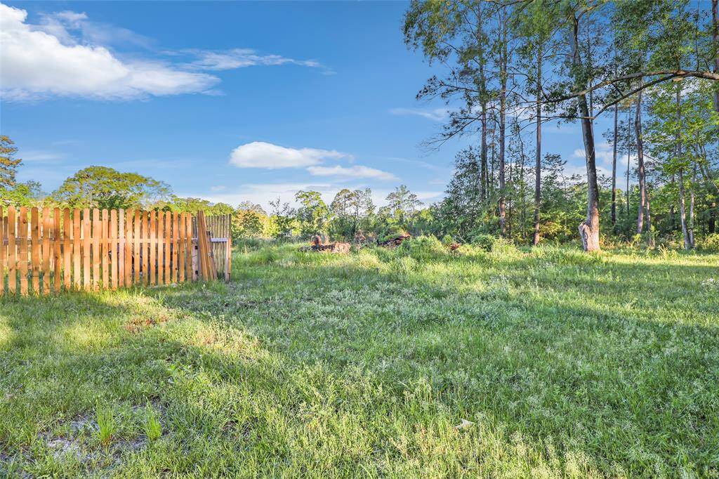 A serene, grassy lot with a wooden fence on one side, surrounded by mature trees, providing a private and natural setting.