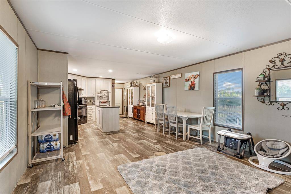 This photo shows a spacious, open-concept living area with a modern kitchen featuring modern appliances and an island. The dining area has a cozy setup with a table and chairs. Neutral tones and wood-look flooring add a warm touch.
