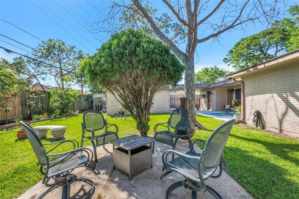 This backyard features a cozy seating area with four chairs surrounding a small fire pit, set on a concrete patio. The space is surrounded by a well-maintained lawn and mature trees, offering a tranquil, private setting.