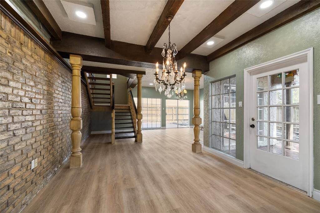 The formal dining area features a central chandelier, large wood beams across the ceiling, and a structural support beam held by custom wood pillars. It offers access to the side courtyard.