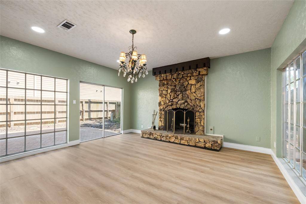 The stone fireplace in the den matches the large arc in the living room, creating a cohesive design. The chandelier above, along with large windows and glass sliding door, fills the room with abundant natural light.