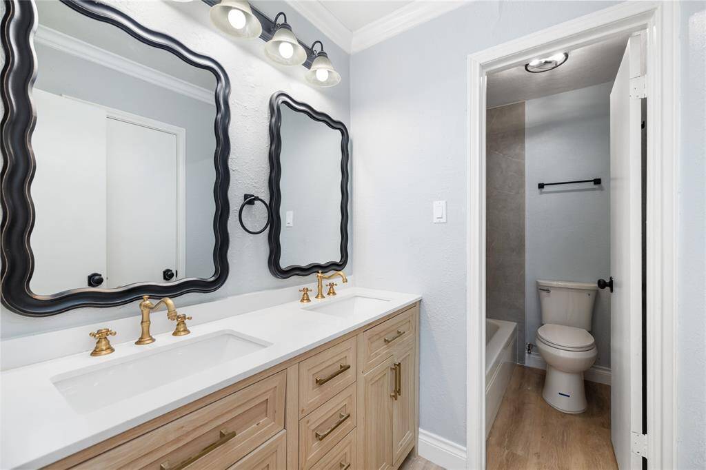 This fully renovated bathroom in the downstairs primary bedroom features a double sink and gold-colored faucets, which are consistent throughout the property. The elegant design and modern updates enhance the space, creating a luxurious and functional retreat.