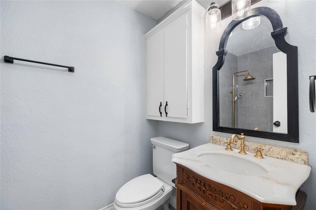 This full bathroom mirrors the style of the primary suite bathroom, featuring a single sink and the same elegant finishes. The shower/tub combo is updated with smooth gray stone tiles, and the gold faucets, consistent throughout the property, add a sophisticated touch to the space.