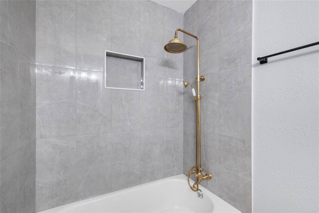 This full bathroom mirrors the style of the primary suite bathroom, featuring a single sink and the same elegant finishes. The shower/tub combo is updated with smooth gray stone tiles, and the gold faucets, consistent throughout the property, add a sophisticated touch to the space.