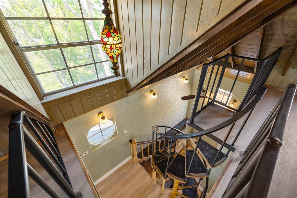 A view from atop the loft on the third floor looks down the custom iron spiral staircase, showcasing its unique design and adding a striking focal point to the space. The open layout of the loft area complements the architectural style of the home.