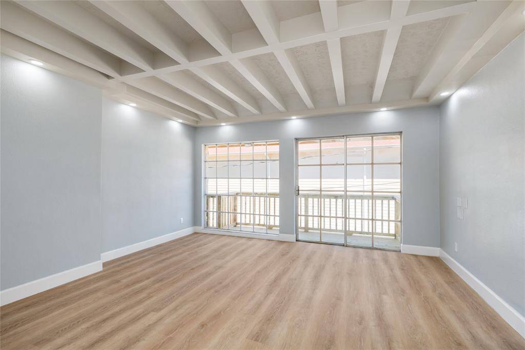 This spacious second-floor room, one of two primary/master bedrooms, features its own bathroom suite and walk-in closet. A custom balcony is accessible via a sliding glass door next to a large window that nearly stretches from floor to ceiling, flooding the room with natural light. The white-painted beams across the ceiling add an elegant architectural touch, enhancing the room's overall charm.