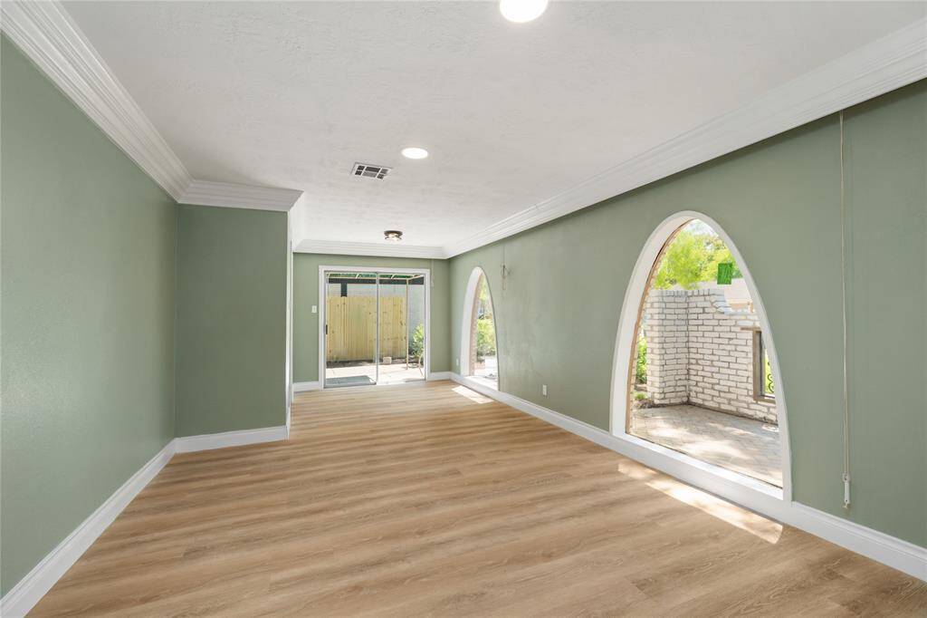 Step into the bright and welcoming receiving room featuring new vinyl wood flooring and stunning arched windows that flood the space with natural light. The updated lighting, including recessed can lights, enhances the airy feel while highlighting the room’s elegant charm.