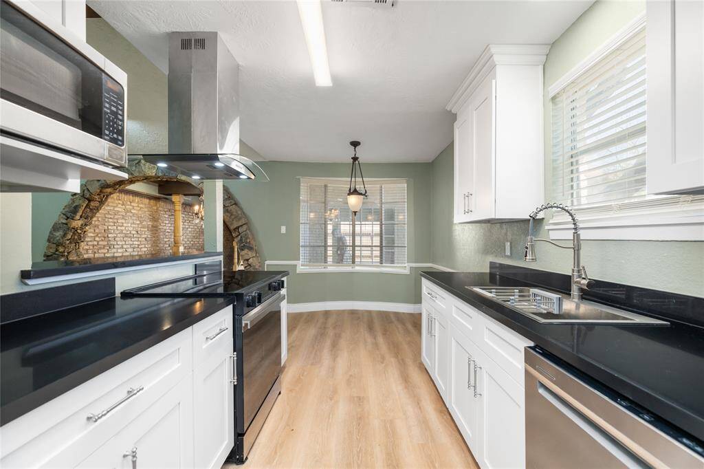 This fully remodeled kitchen offers a seamless view from end to end, accessible directly from the receiving room. Featuring white soft-close cabinets, sleek black countertops, an updated farmhouse sink, and new stainless steel appliances. Dual countertops on both sides provide ample workspace. At the far end, the breakfast area opens beautifully into the living room, creating a bright, open-concept flow.