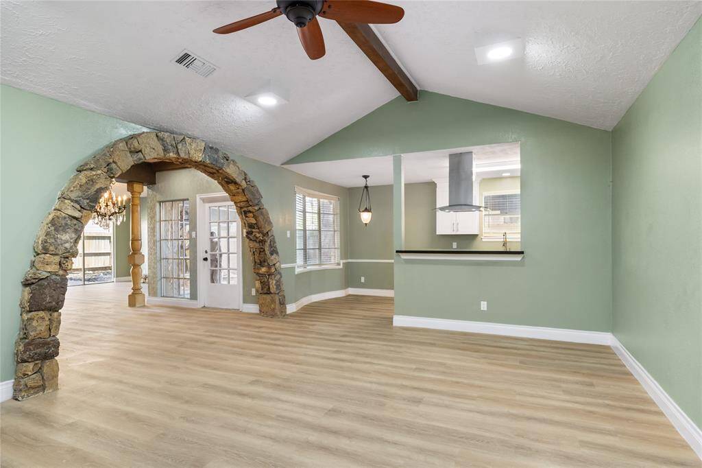 This spacious living room is filled with natural light, thanks to numerous windows and an open layout. At the far end, you can see the breakfast area and kitchen’s breakfast bar. A striking stone arch on the left leads into the formal dining room, which looks out onto a charming courtyard. High ceilings with a prominent wood beam and a new ceiling fan add both character and comfort to this bright, inviting space.